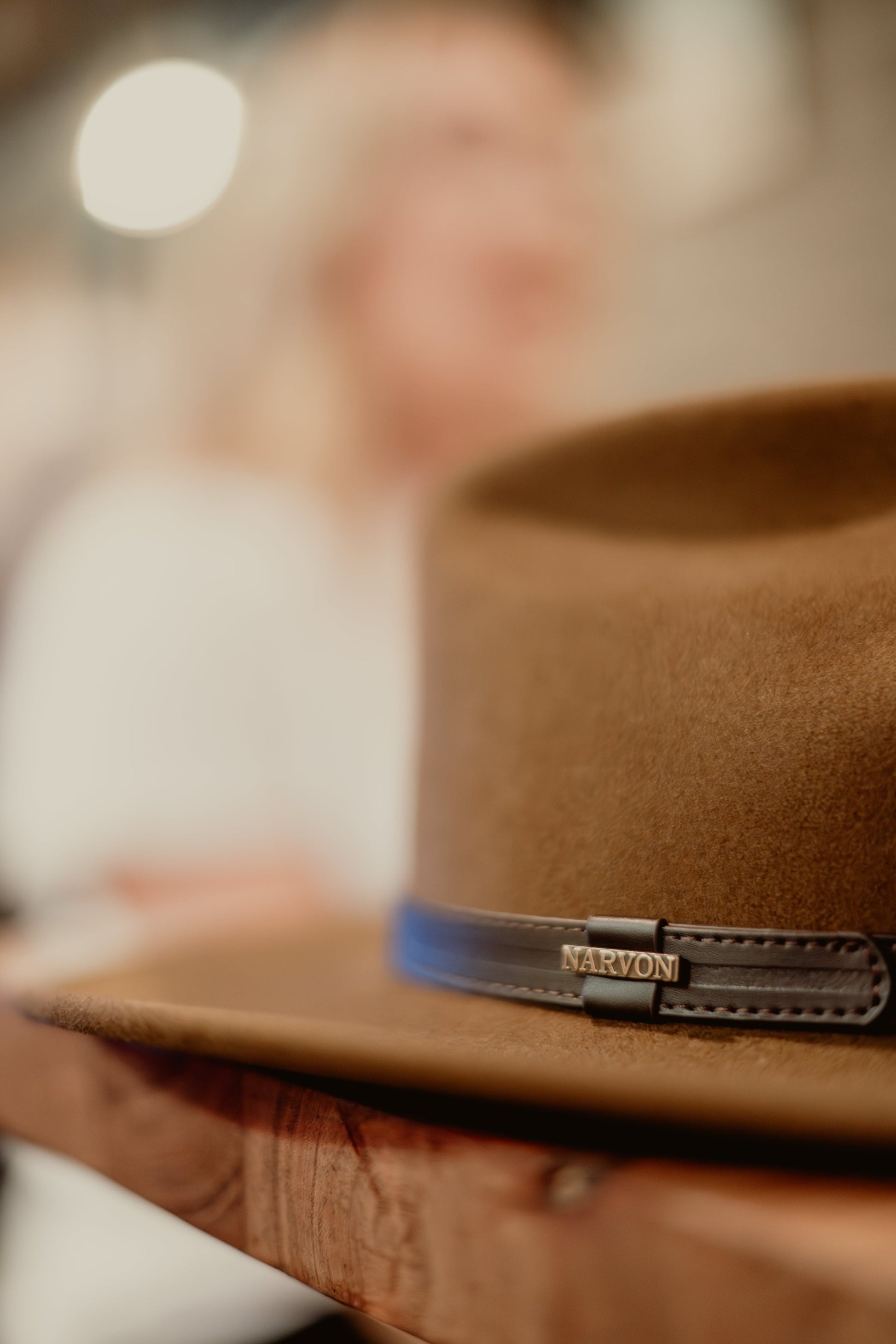 Brown cowboy hat with leather band resting on wooden shelf, western style felt hat lifestyle shot