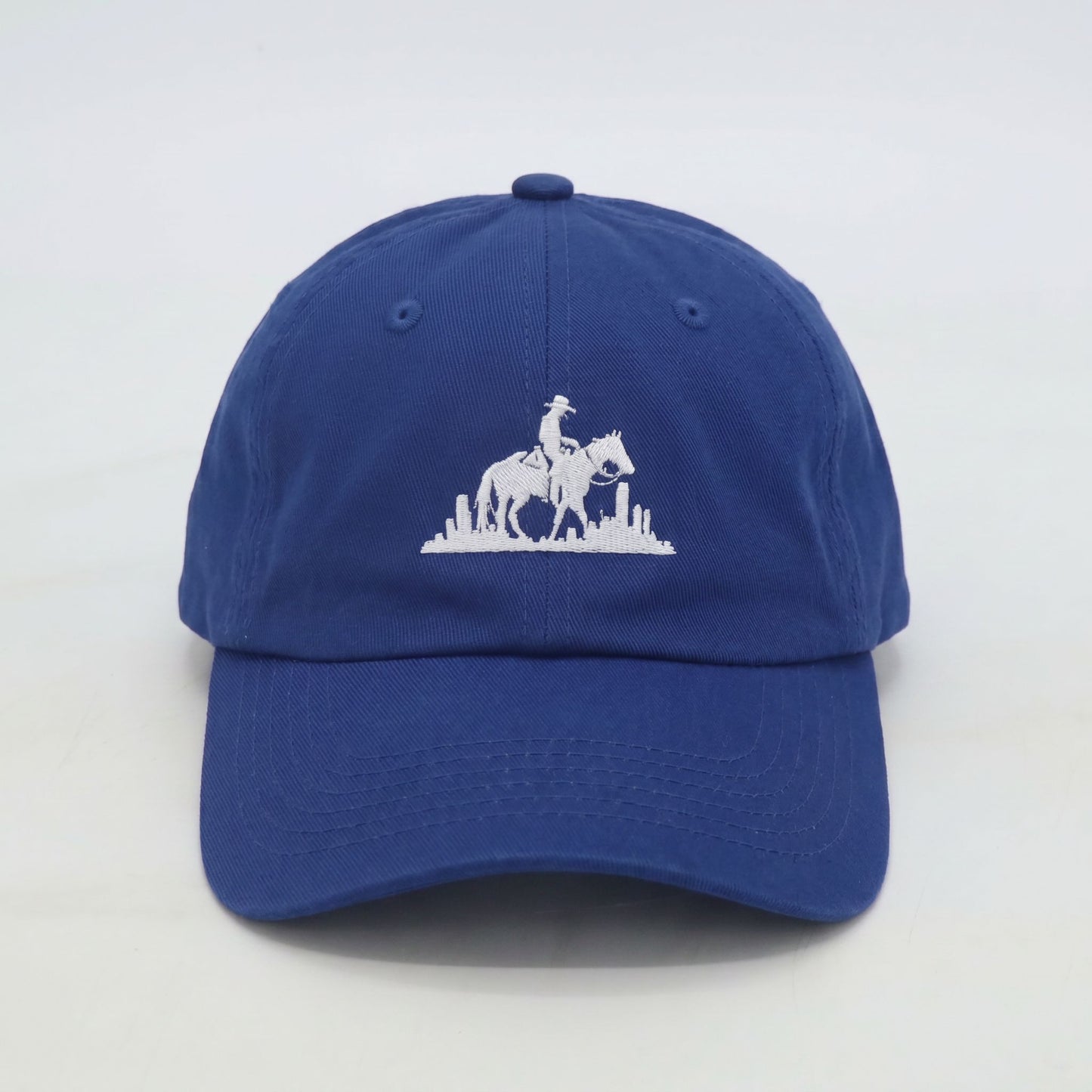 Front view of men’s royal blue dad cap with embroidered rider logo and city backdrop