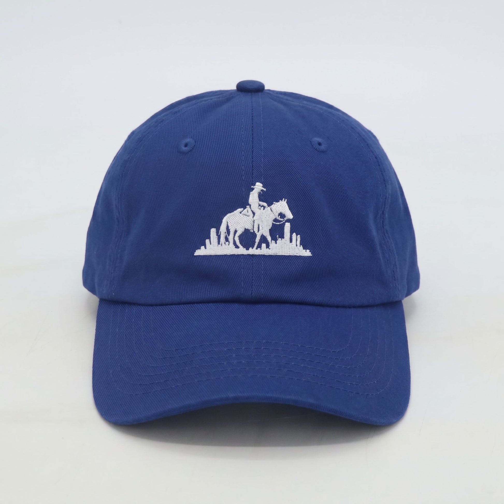 Front view of men’s royal blue dad cap with embroidered rider logo and city backdrop
