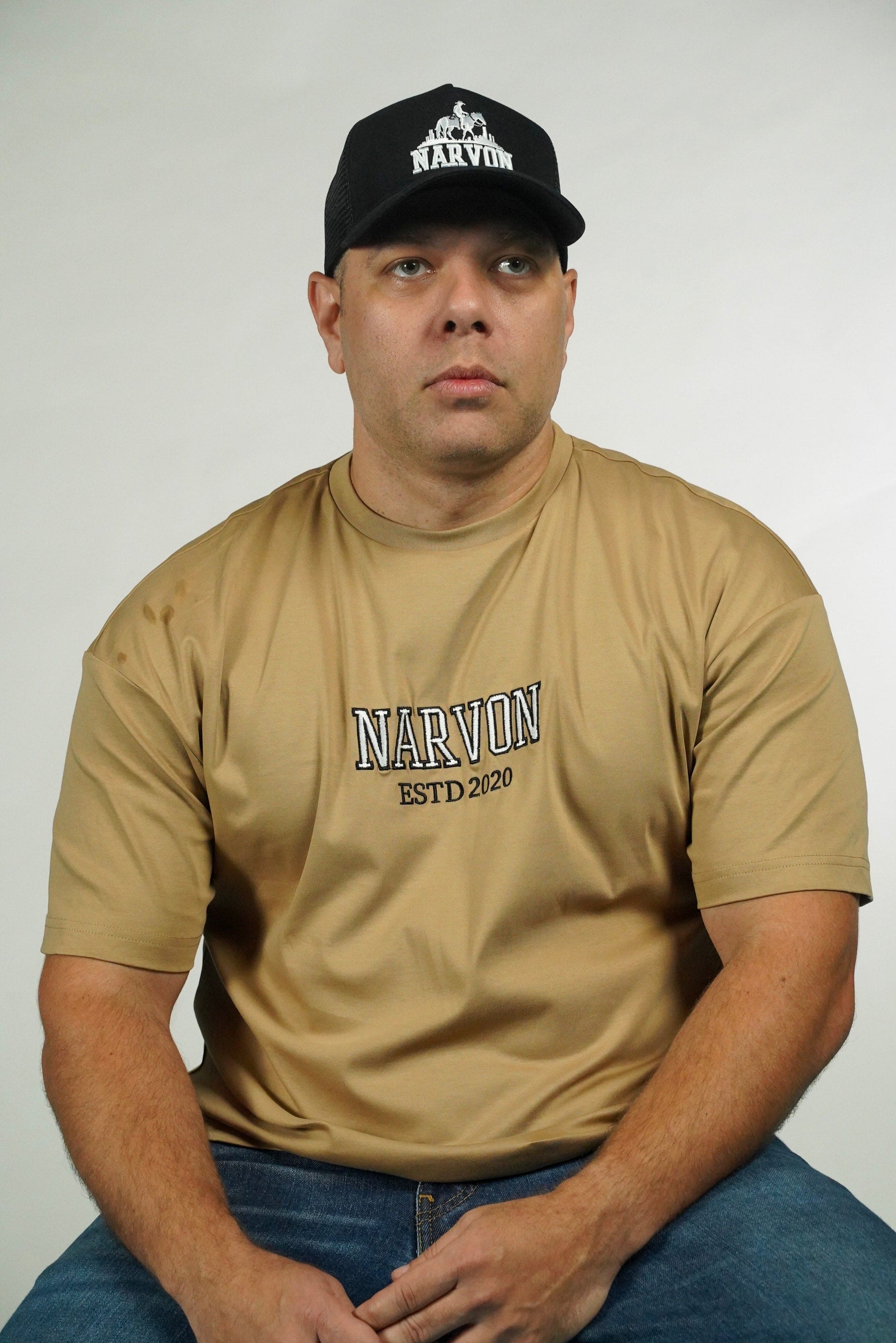 Man wearing a tan 'Narvon' t-shirt and black cap with 'Narvon' logo on a white background